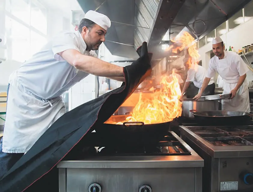 Fire blankets find a logical home in large, industrial kitchens. The advantages are both obvious and profound: They are a quick, clean means of snuffing out fire before it can gain ground. Still, putting out grease fires is said to get a little tricky, as flammable liquid can splash onto the blanket itself and require special handling. Note the way this cook is using the blanket to protect his hands.