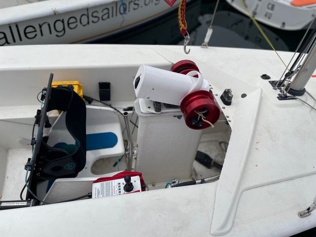 The PAU unit allows steering and sheet control with gentle pressure from just one finger on the joystick. The red windlass drums handle the jib and main sheets. The yellow battery on port side provides power to the adaptive unit. Straps on the seat secure the sailor, who may not be able to sit safely without assistance. (Photo/ Jane Dunn)