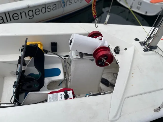The PAU unit allows steering and sheet control with gentle pressure from just one finger on the joystick. The red windlass drums handle the jib and main sheets. The yellow battery on port side provides power to the adaptive unit. Straps on the seat secure the sailor, who may not be able to sit safely without assistance. (Photo/ Jane Dunn)