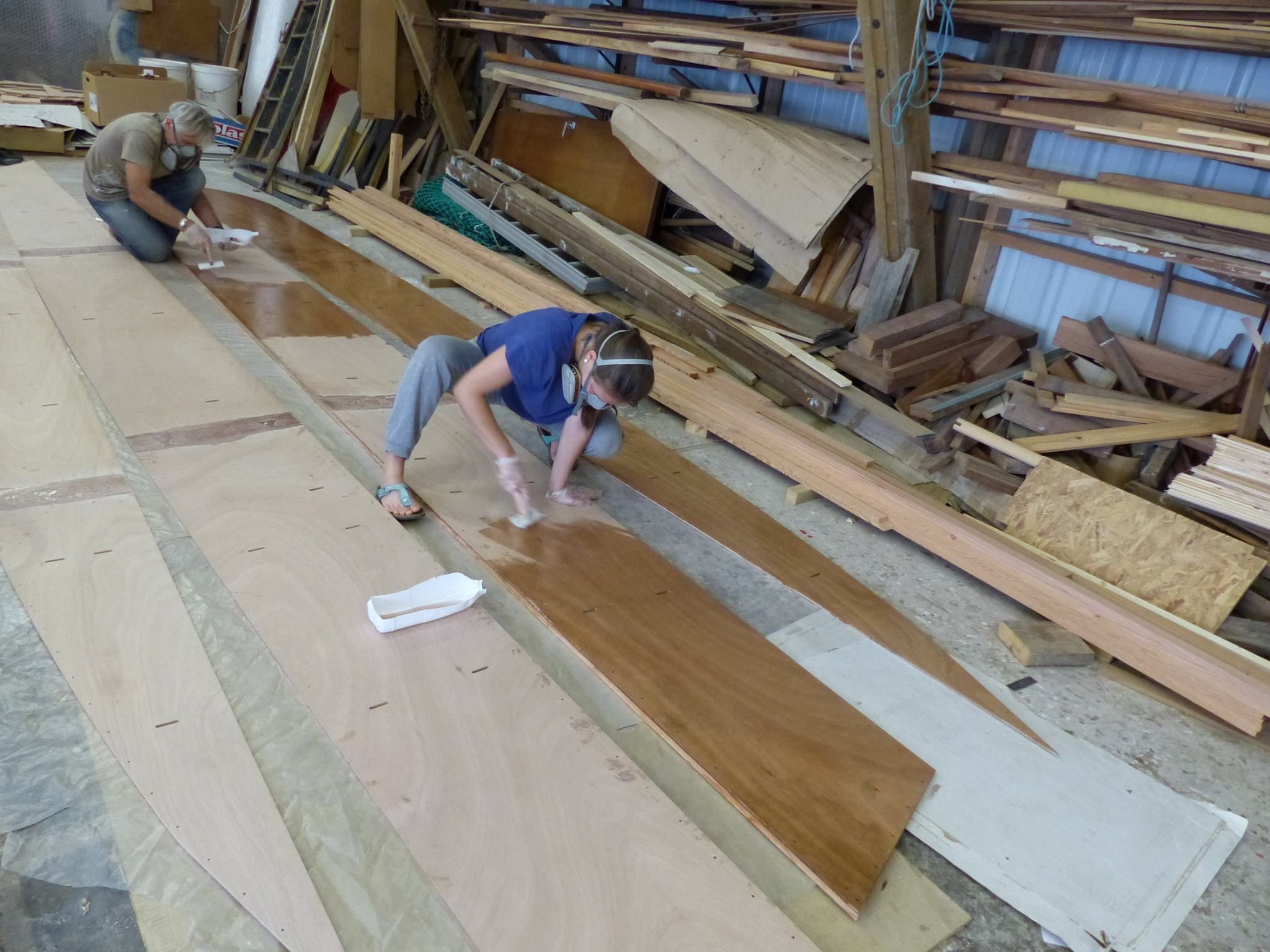 Coating the large surfaces of the hull sides is also done with the paint pads, as quick as using a roller and it does not create as many air bubbles. We use vapor masks as the epoxy does give off toxic fumes, particularly when coating large surfaces. (Photo/ Wharram Designs)