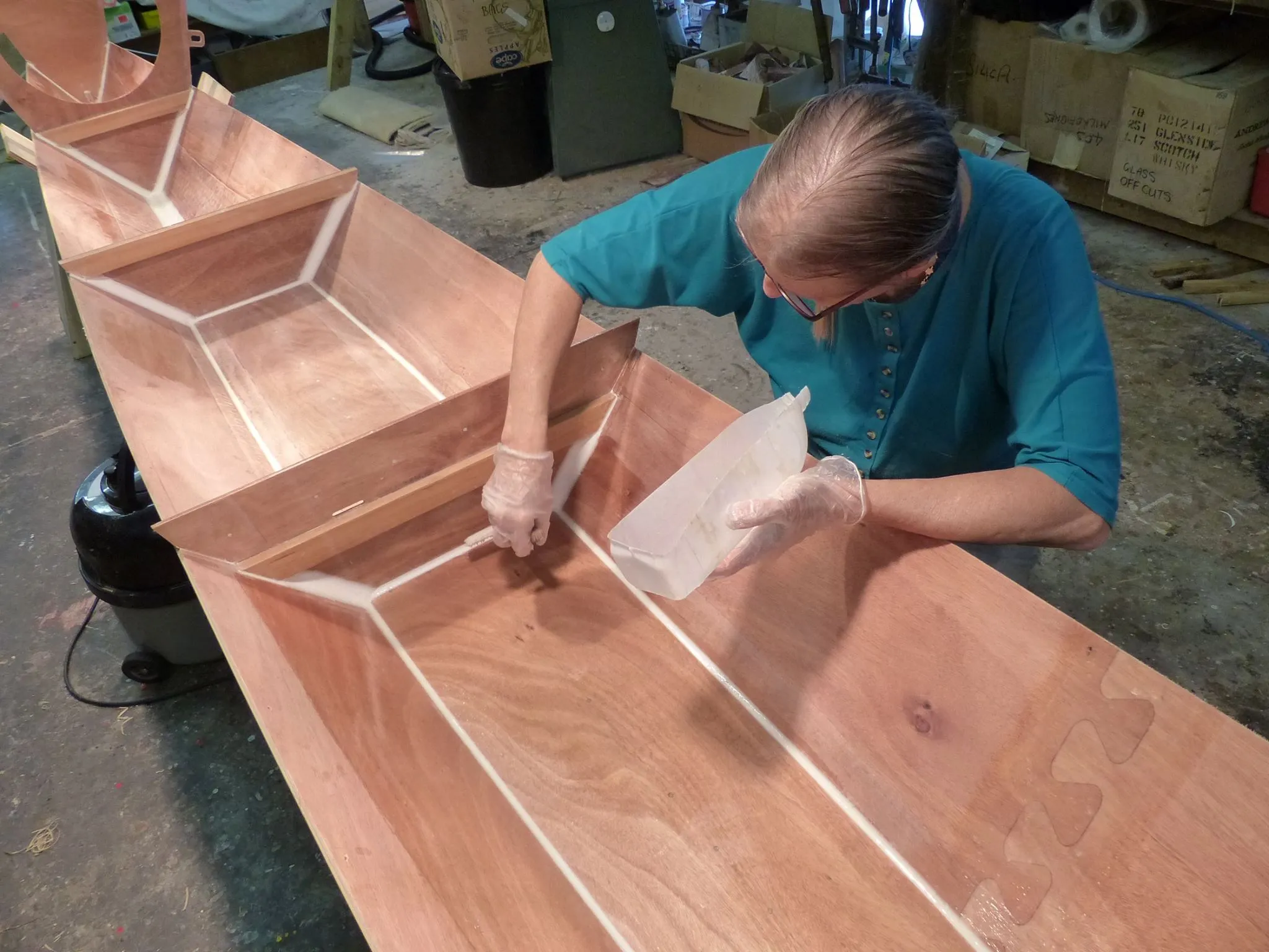 The floor is filleted and glassed over. Hanneke is applying a second coat of epoxy, again using the spreader cut from a roller sleeve. (Photo/ Wharram Designs)