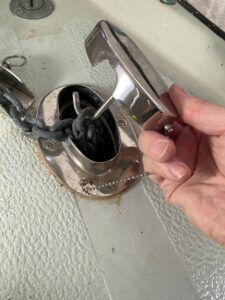 A hawse pipe and chain lock installed on the author’s Albin Ballad 30. A retaining chain keeps the pipe cover from going over the side while a hook employs the weight of the chain to keep the cover secured over the pipe. (Photo/ Doug Henschen)