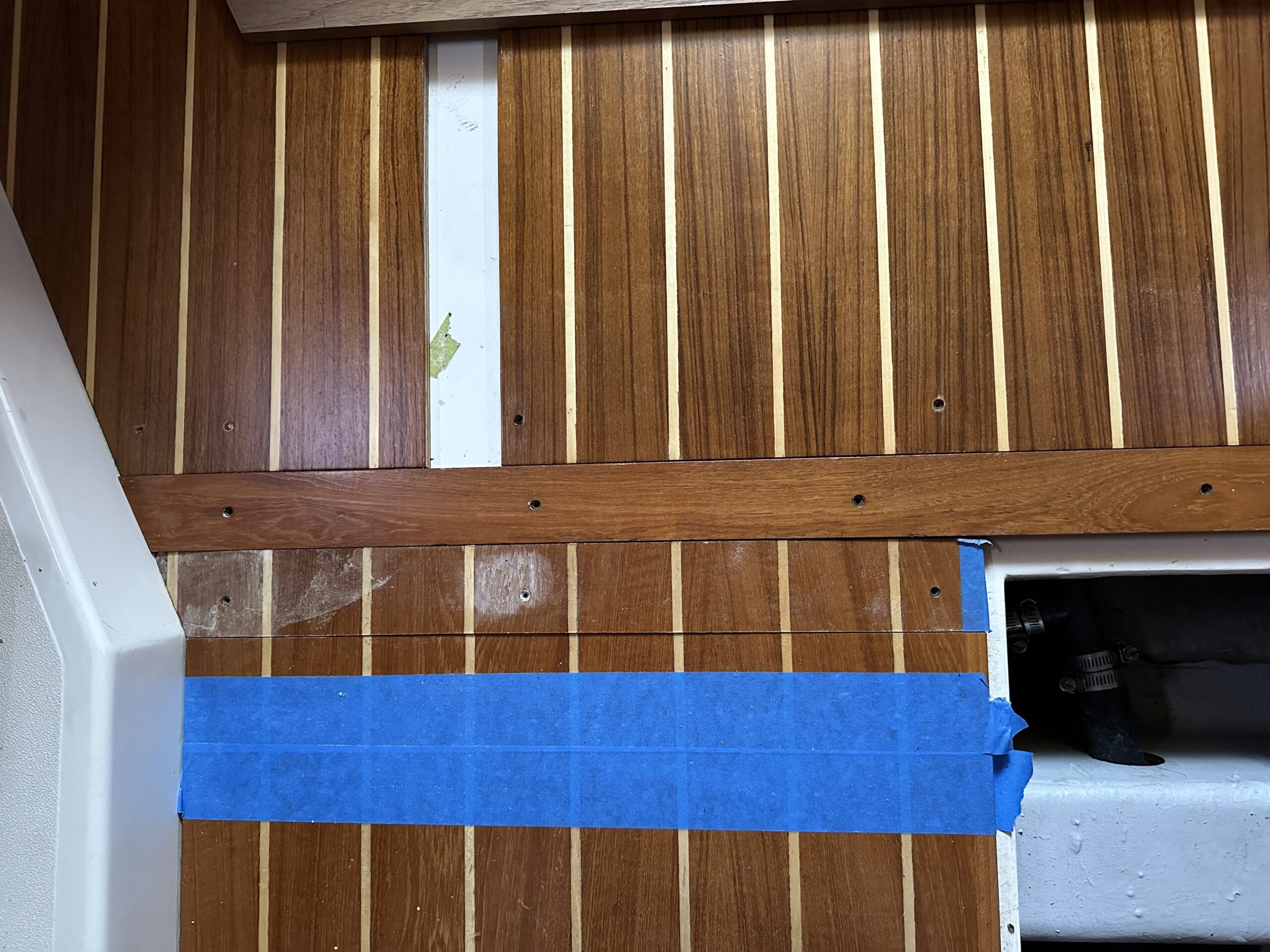 With four coats of satin varnish the revitalized panels are re-fitted. The small portion of the long panel at the bottom of the photo (towards the bow) which was also damaged is to be cut out. The blue masking tape is applied to protect the good sole. (Photo/ Bert Vermeer)