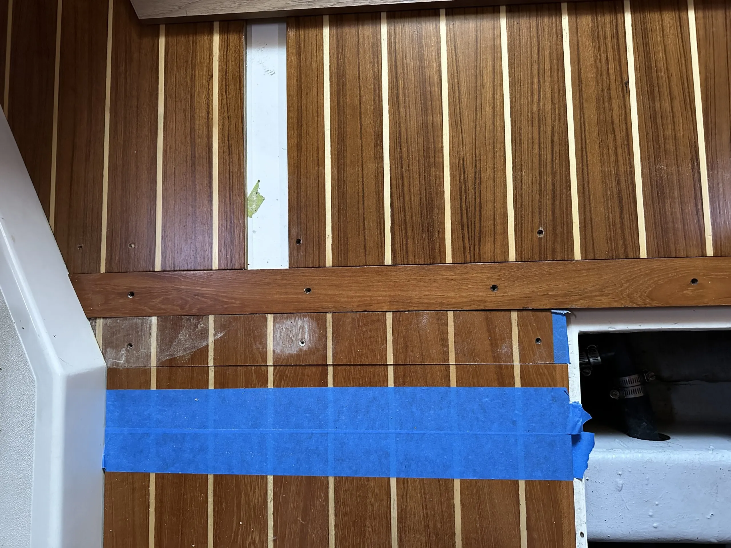 With four coats of satin varnish the revitalized panels are re-fitted. The small portion of the long panel at the bottom of the photo (towards the bow) which was also damaged is to be cut out. The blue masking tape is applied to protect the good sole. (Photo/ Bert Vermeer)