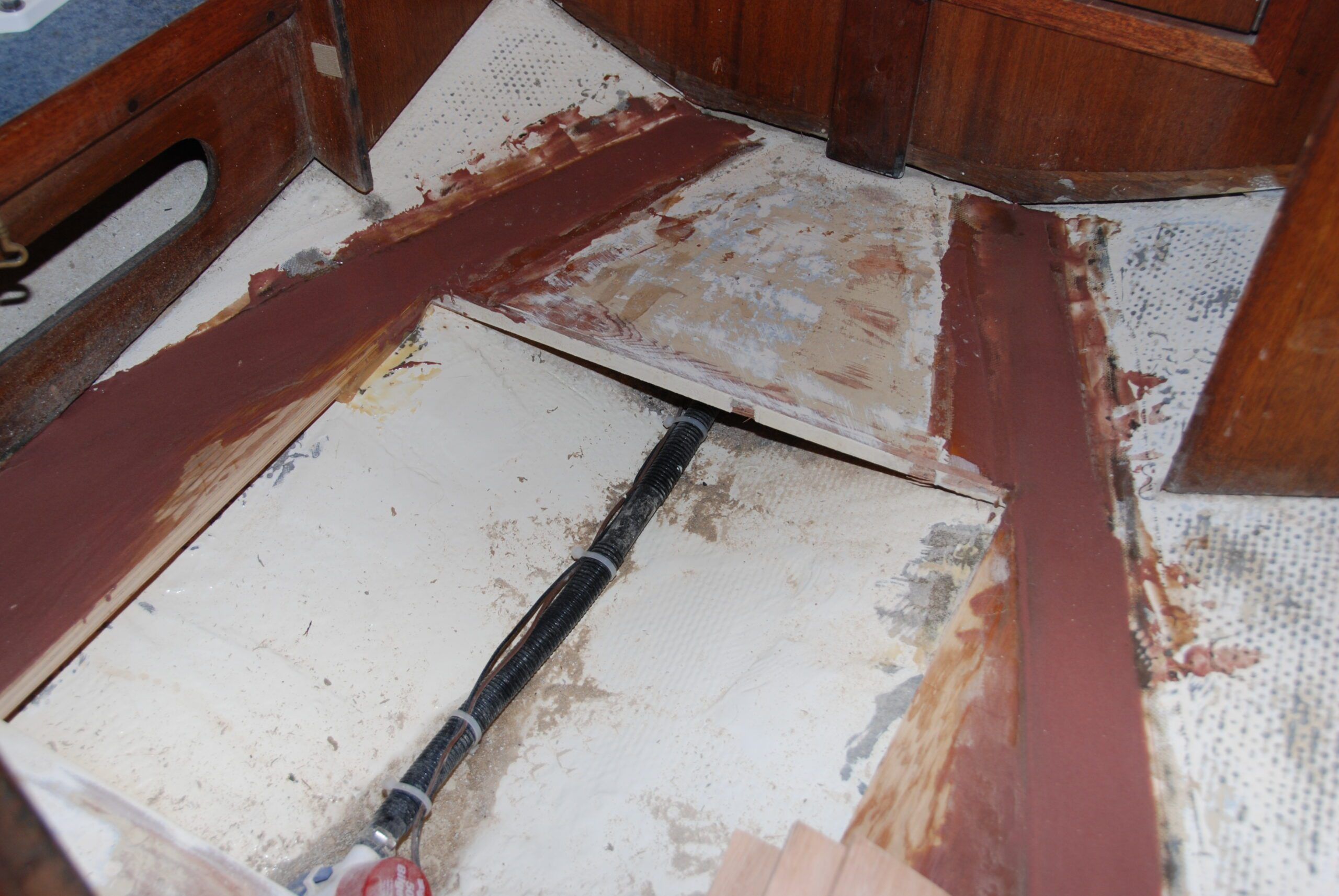 Fairing the plywood to fiberglass hull joint with thickened West System epoxy. In the head, the plywood has been cut for the future shower grate, the shower sump pump installed. (Photo/ Bert Vermeer)