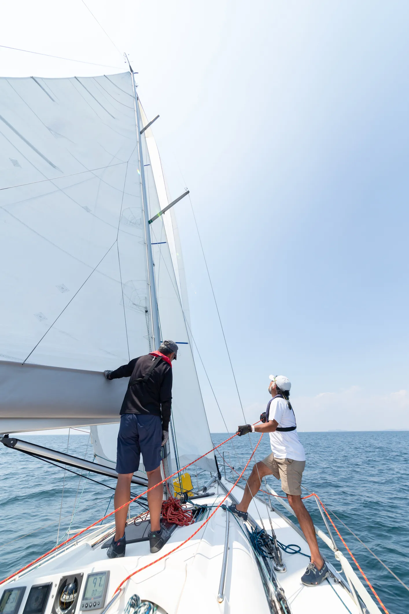 These sailors are wearing lifejackets and have proper footwear. Even though the sailor is focused on the sail trim, they also have their feet placed to brace for a potential heel.