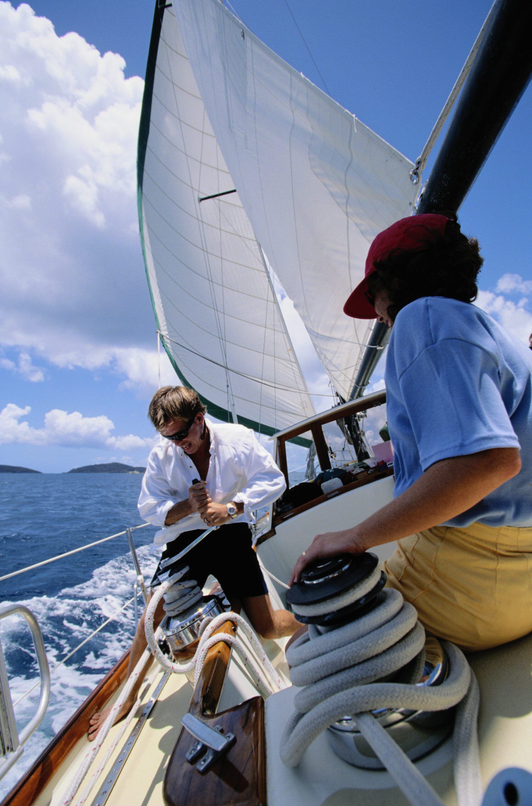 While these sailors are not wearing lifejackets, the one on the winch is making good use of the toe rail.