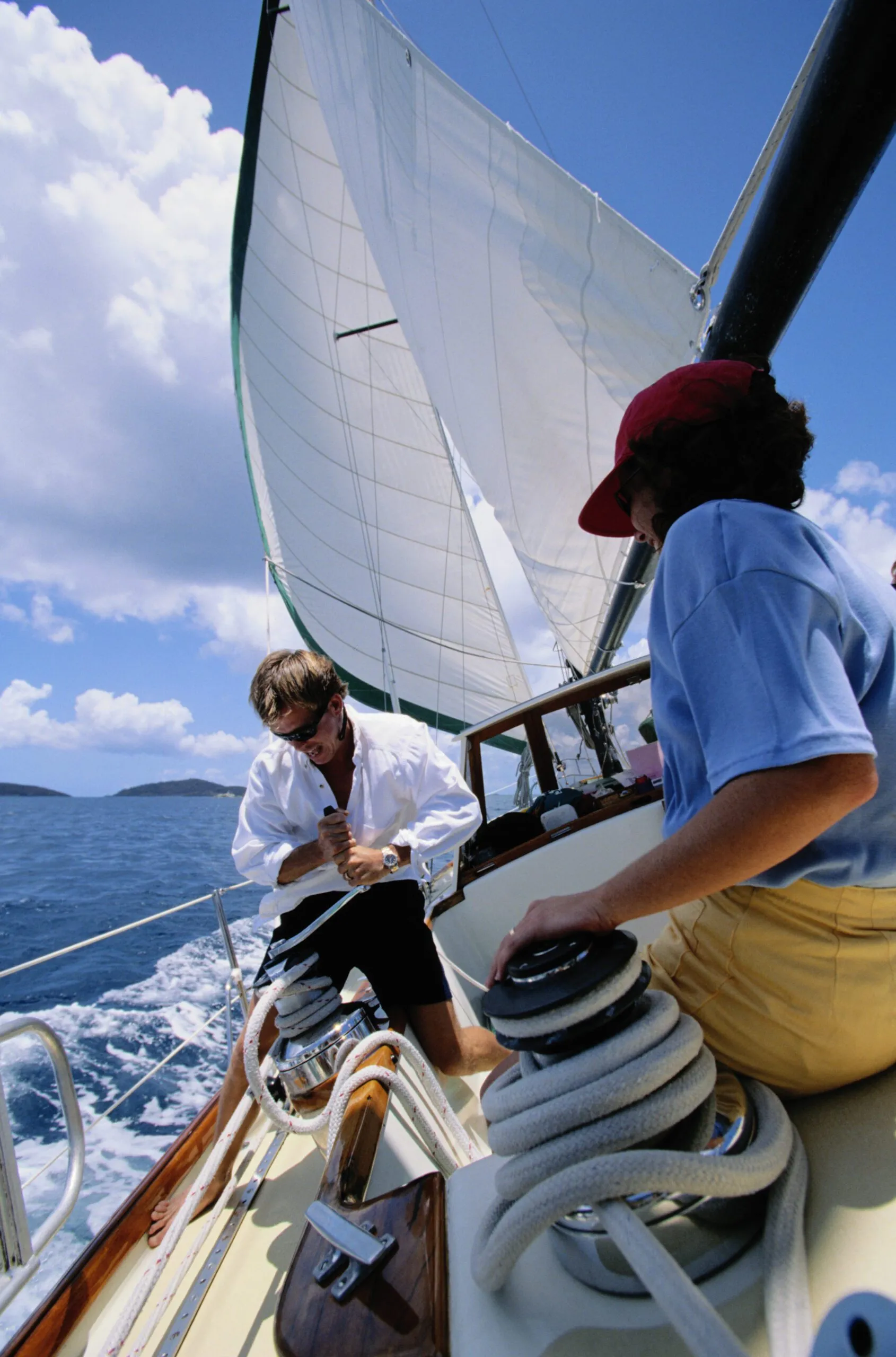 While these sailors are not wearing lifejackets, the one on the winch is making good use of the toe rail.