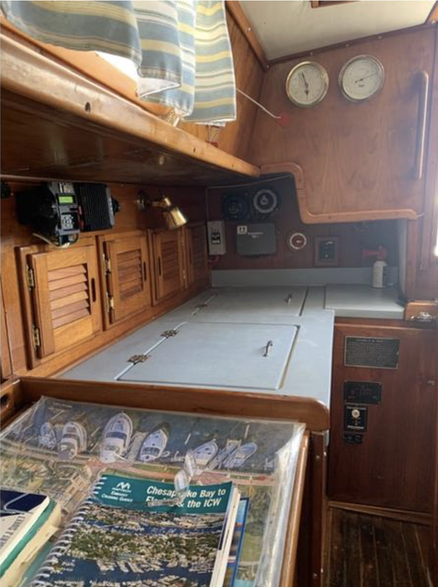 The starboard galley features traditional louvered cabinet doors and ample storage, though the sink positioned below the companionway and limited counter space reflect the modest standards of the era. The two-burner stove and icebox offer basic provisions for coastal cruising, with many owners upgrading to propane and adding insulation to improve functionality. Courtesy of SailboatListings.com