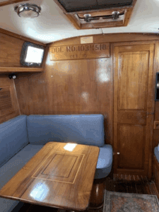 The main saloon features a U-shaped settee to port and a straight settee with pilot berth above to starboard, surrounding a traditional teak dinette table. The builder's plate on the bulkhead documents this boat's construction at Morgan Yachts in St. Petersburg, Florida, where approximately 350 hulls were built between 1967 and 1972. Courtesy of SailboatListings.com