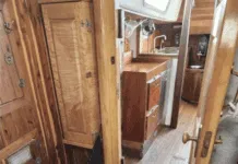 The companionway and main cabin entrance showcases classic teak joinery throughout, with abundant storage lockers, a spacious galley to starboard, and traditional teak-and-holly sole. The deep companionway sill provides a secure threshold for offshore passages. Courtesy of SailboatListings.com