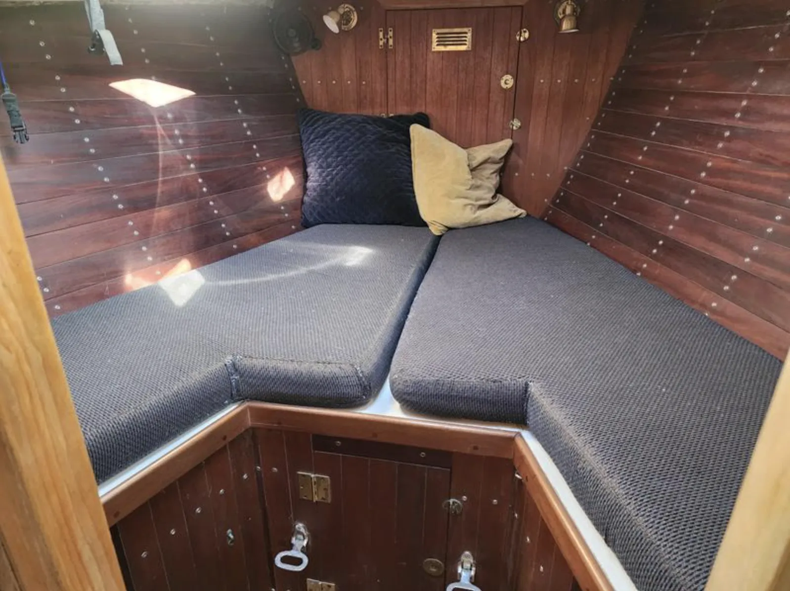 The V-berth stretches approximately 6 ft., 11 in. and features stick-built construction with traditional wood paneling secured by visible fasteners. The large forward hatch provides natural light and ventilation, while the offset centerboard trunk to port adds character to this classic cruiser-racer layout. Courtesy of SailboatListings.com