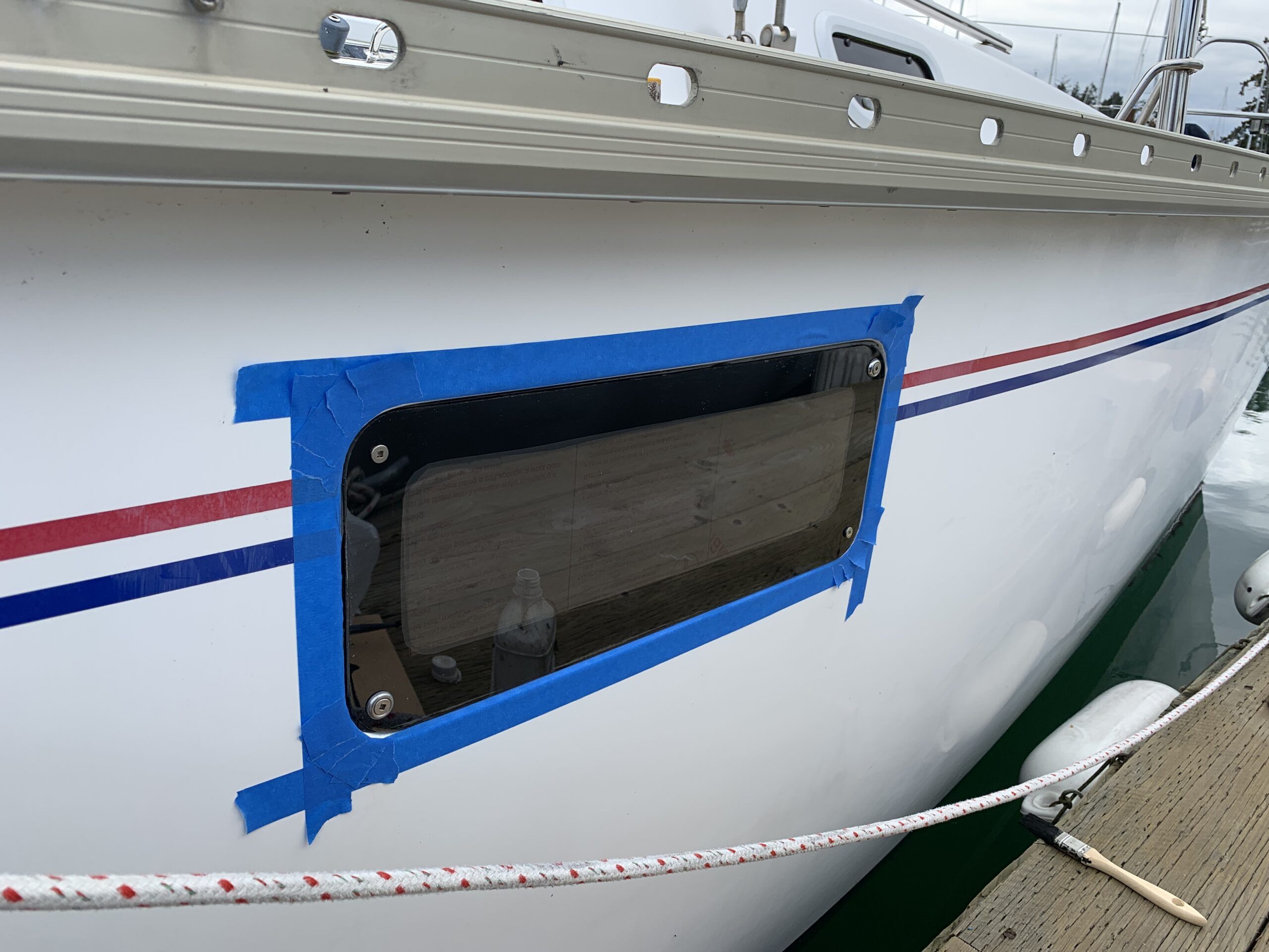 These portlights have screws holding the plexiglass in place. Masking tape is applied to protect the surrounding gelcoat from the soon-to-be-applied black filler Sikaflex. (Photo/ Bert Vermeer)