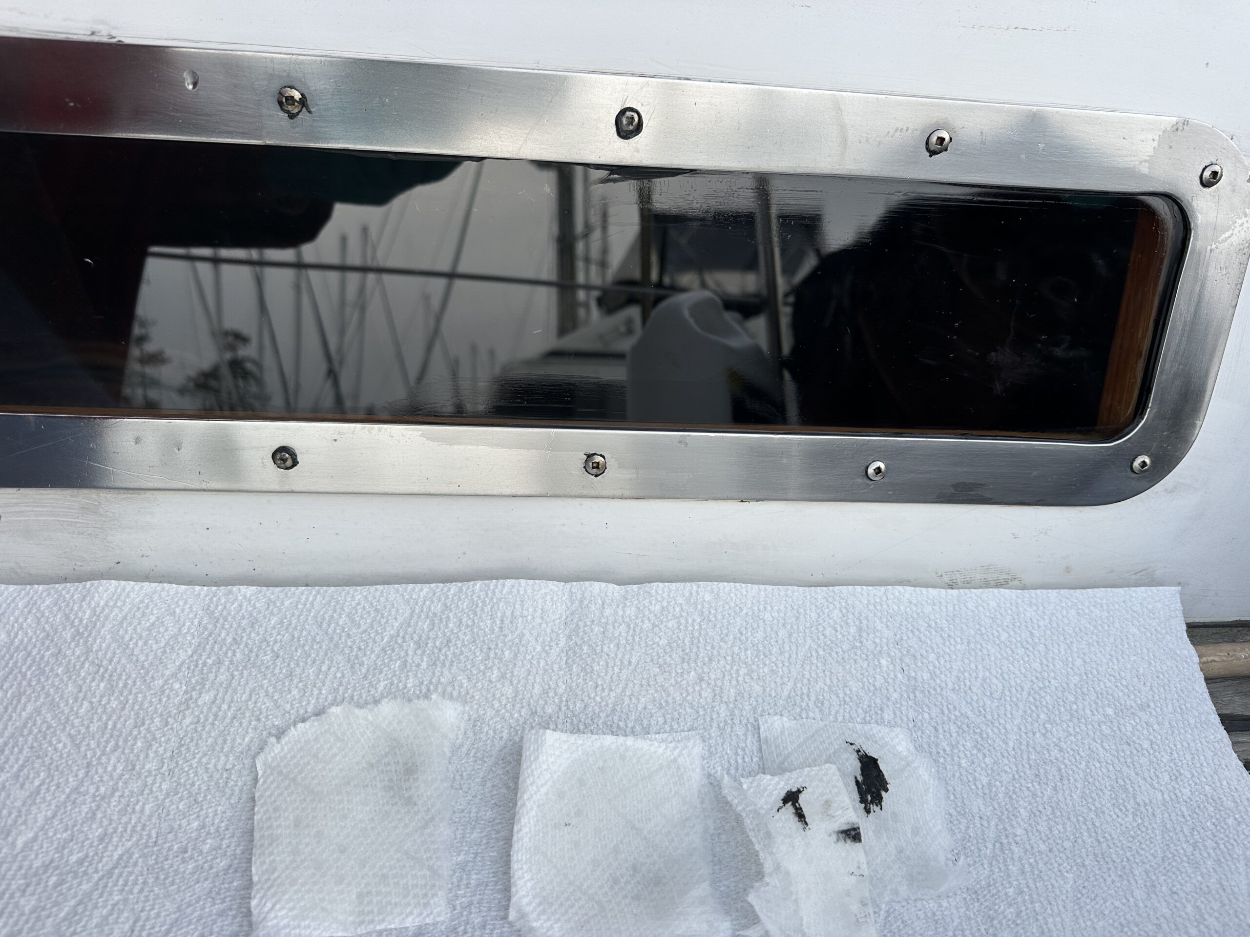 The SS metal frame is in place. The installation screws show traces of black Sikaflex. Note the small squares of paper towels dampened with solvent to clean the excess sealer. (Photo/ Bert Vermeer)
