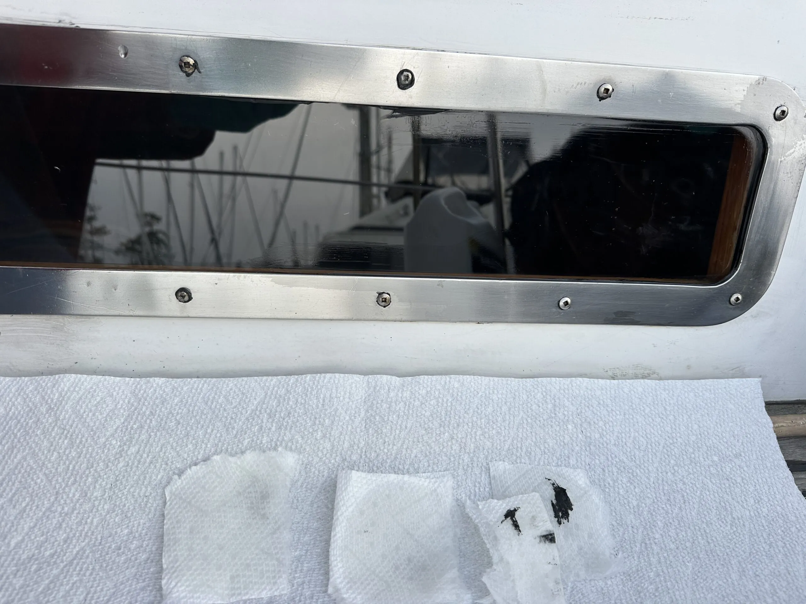 The SS metal frame is in place. The installation screws show traces of black Sikaflex. Note the small squares of paper towels dampened with solvent to clean the excess sealer. (Photo/ Bert Vermeer)