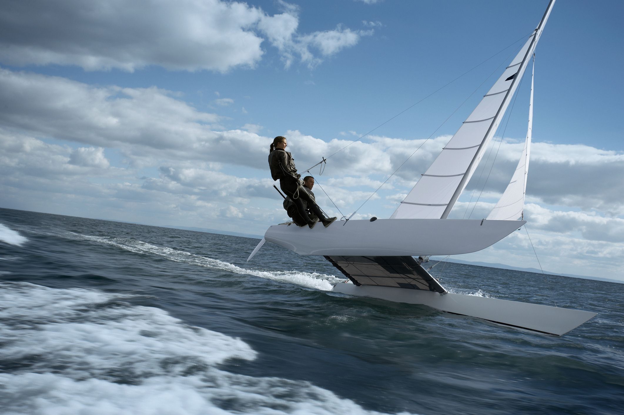 A high-performance catamaran demonstrates massive initial stability, flying a hull while the crew manages the heeling moment. While multihulls offer immense resistance to heel at low angles, their GZ curve is unforgiving—once the angle of vanishing stability is reached (often much sooner than a monohull), the righting moment disappears abruptly.