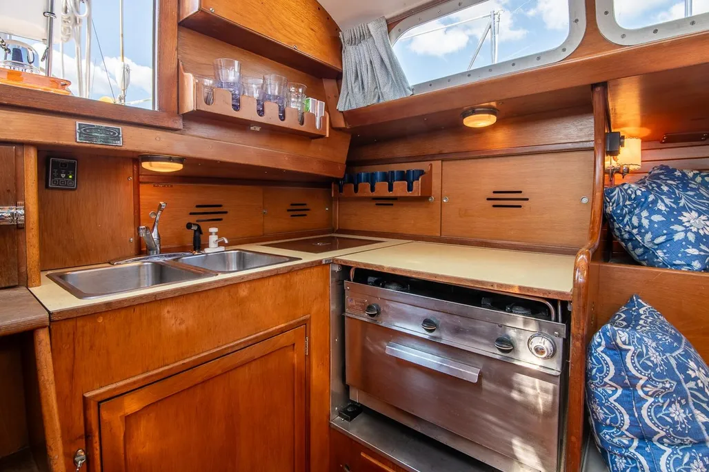 The compact aft galley pairs with a navigation station positioned above the starboard icebox, though owners note the standing-only arrangement limits extended passagemaking comfort. Courtesy of YachtWorld.com
