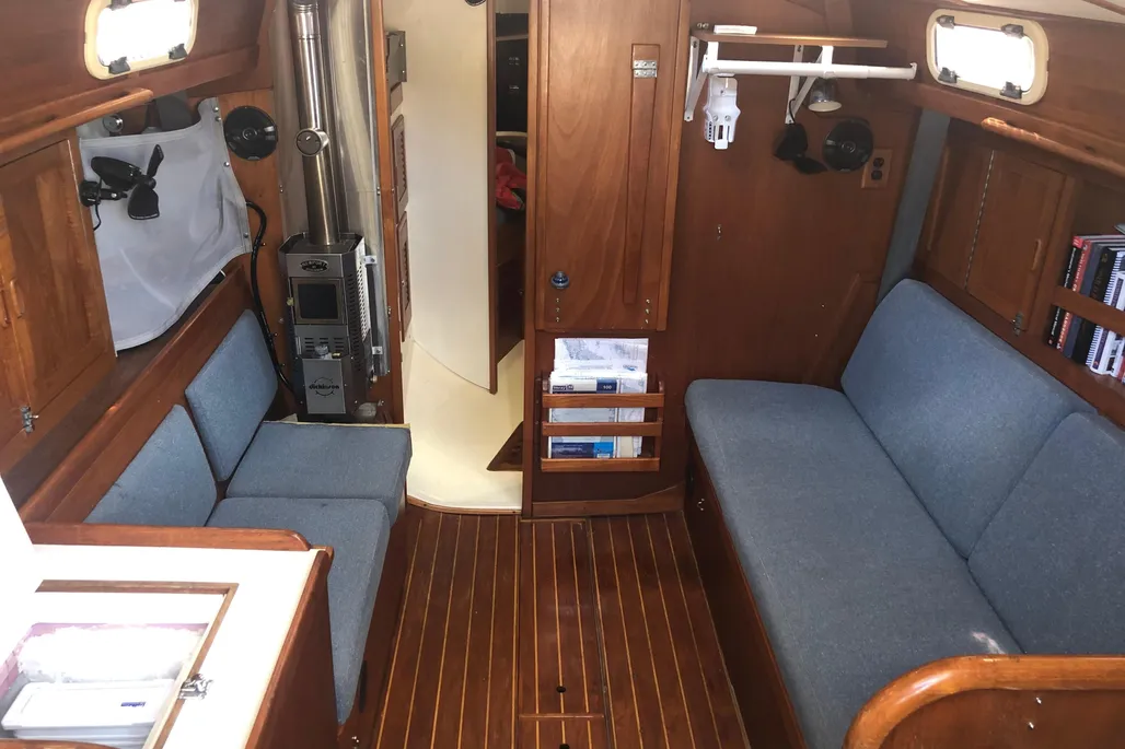 The saloon layout puts the short port settee opposite a full-length berth, with a bulkhead heater eating into already tight space. It works at sea, but the cramped seating confirms this is more cruiser-racer than floating condo. (Photo courtesy of YachtWorld.com)