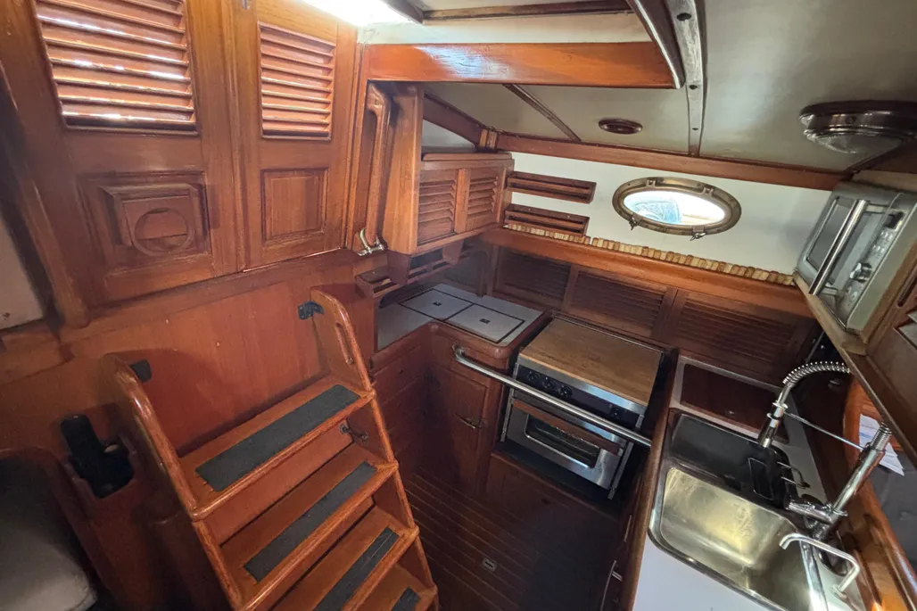 The companionway ladder leads down to the galley, with the engine compartment accessible below the cockpit sole via removable panels. The louvered teak doors throughout are typical of the era but require regular upkeep—a recurring theme with any Union 36.(Photo courtesy of YachtWorld.com)