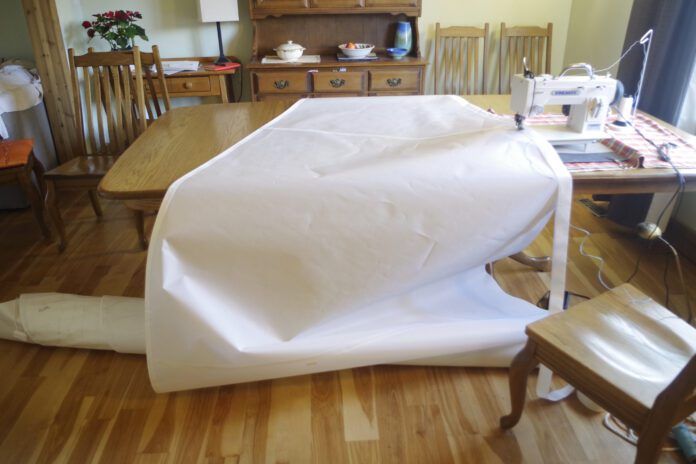 The longest seams are the edges. You can do these by running the sail over the table as you do not need to roll the cloth on the side that is passing through the throat. The sail is rolled crossways so that one side is unrolling, and the opposite side is rolling up. Just make sure the cloth does not snag as it moves across the table. You could do this on the floor as well, but it is much more comfortable to work sitting at a table when you can.