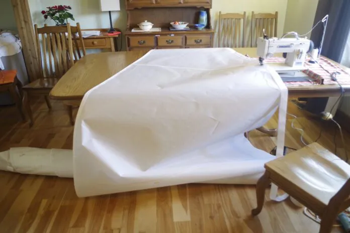 The longest seams are the edges. You can do these by running the sail over the table as you do not need to roll the cloth on the side that is passing through the throat. The sail is rolled crossways so that one side is unrolling, and the opposite side is rolling up. Just make sure the cloth does not snag as it moves across the table. You could do this on the floor as well, but it is much more comfortable to work sitting at a table when you can.